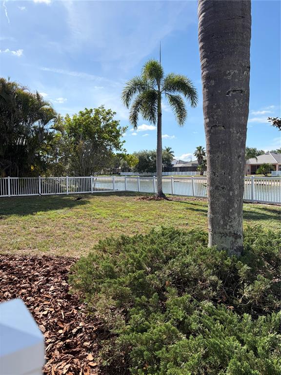 A backyard features a white fence, a palm tree, and a pond under a blue sky — 7779 AROLLA PINE BOULEVARD, SARASOTA, FL