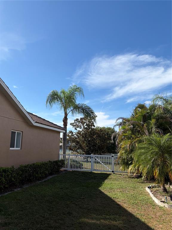 A view of a tan house exterior with a white fence, palm trees, and lawn — 7779 AROLLA PINE BOULEVARD, SARASOTA, FL
