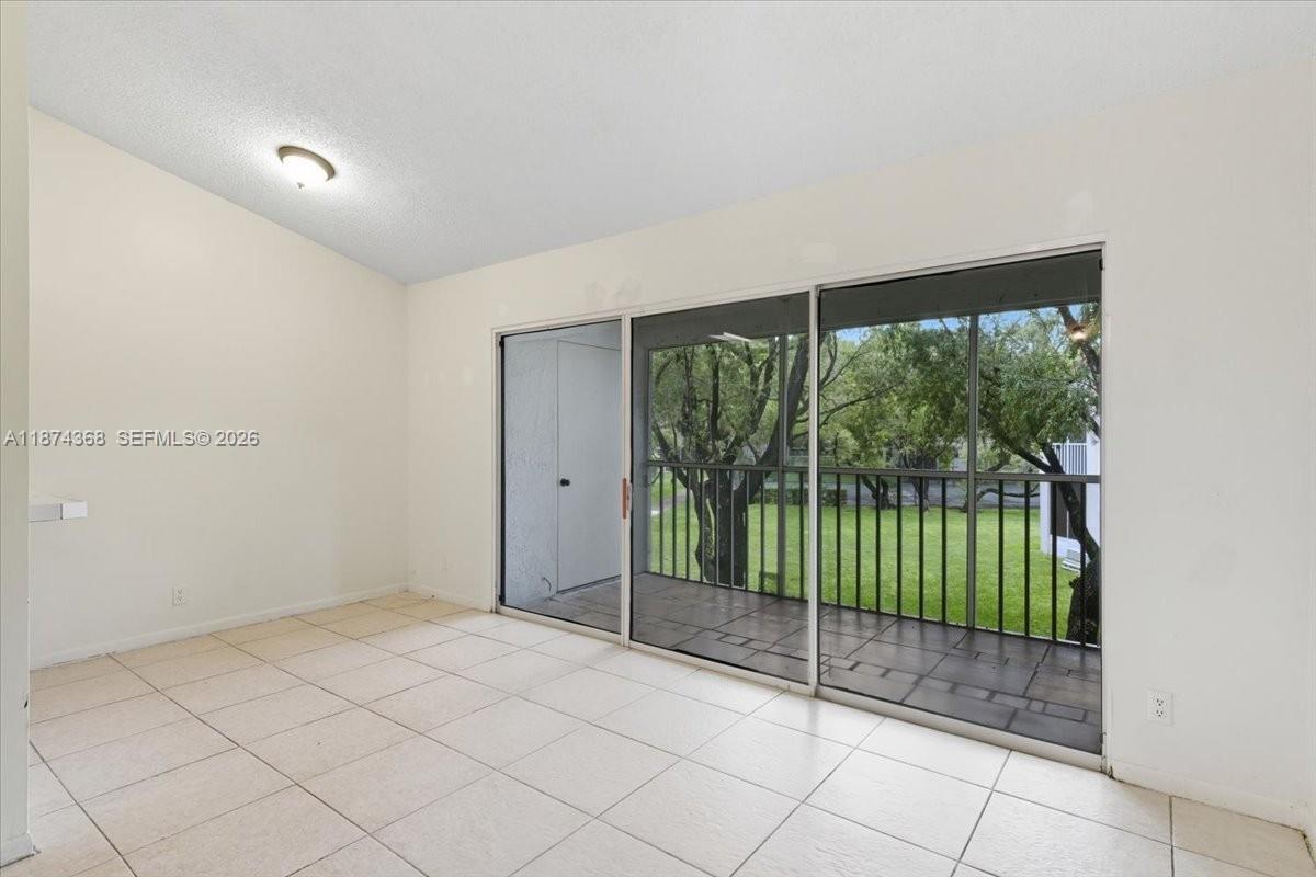 An empty room features white tile flooring, a vaulted ceiling, and sliding glass doors to a balcony — 9167 SW 138th Pl # 9167, Miami FL 33186, MIAMI, FL