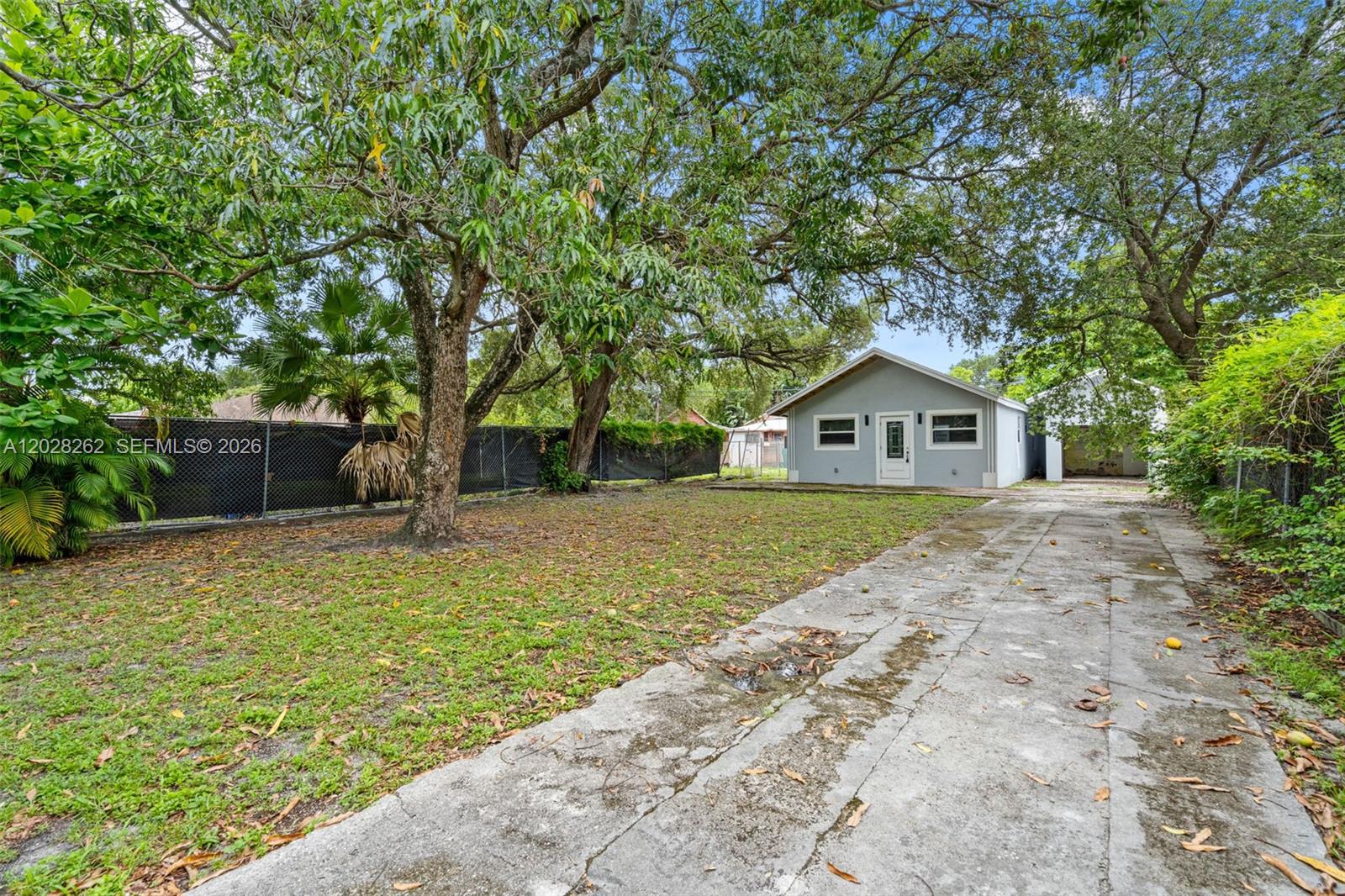 A light gray house with a white door sits behind a concrete driveway and trees — 352 NW 41st St, Miami FL 33127, MIAMI, FL