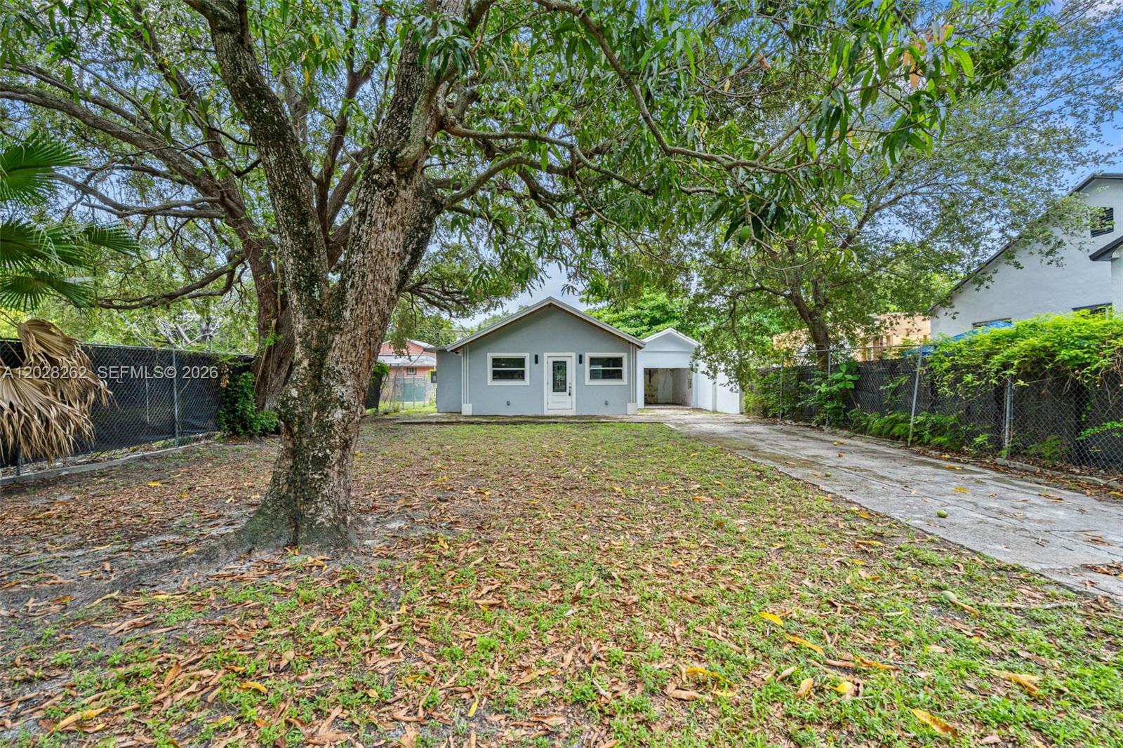 A gray house with a white door and a driveway sits behind a large tree — 352 NW 41st St, Miami FL 33127, MIAMI, FL
