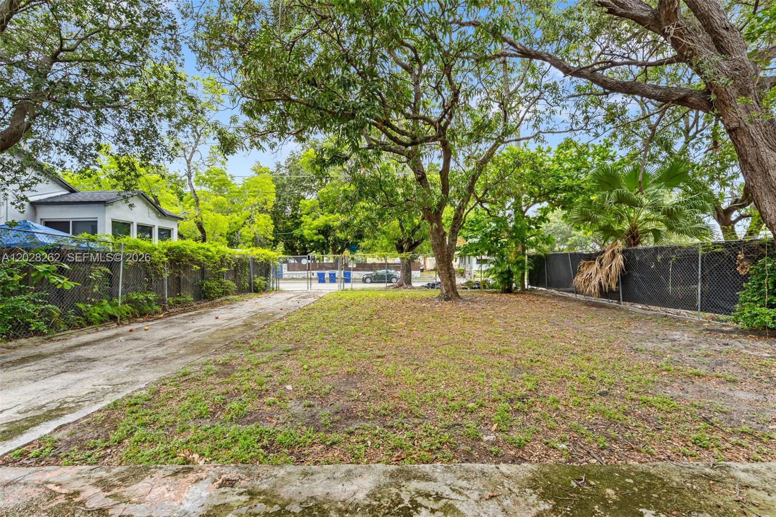 A fenced, grassy lot features a concrete driveway and several large trees — 352 NW 41st St, Miami FL 33127, MIAMI, FL