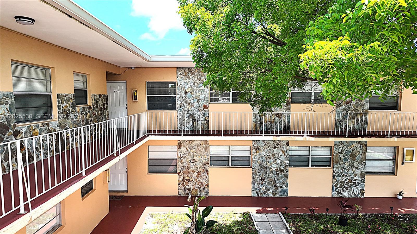 A two-story apartment building features tan stucco walls, stone accents, and a white metal railing — 31 SE 2nd Ave # 203, Hallandale Beach FL 33009, HALLANDALE BEACH, FL