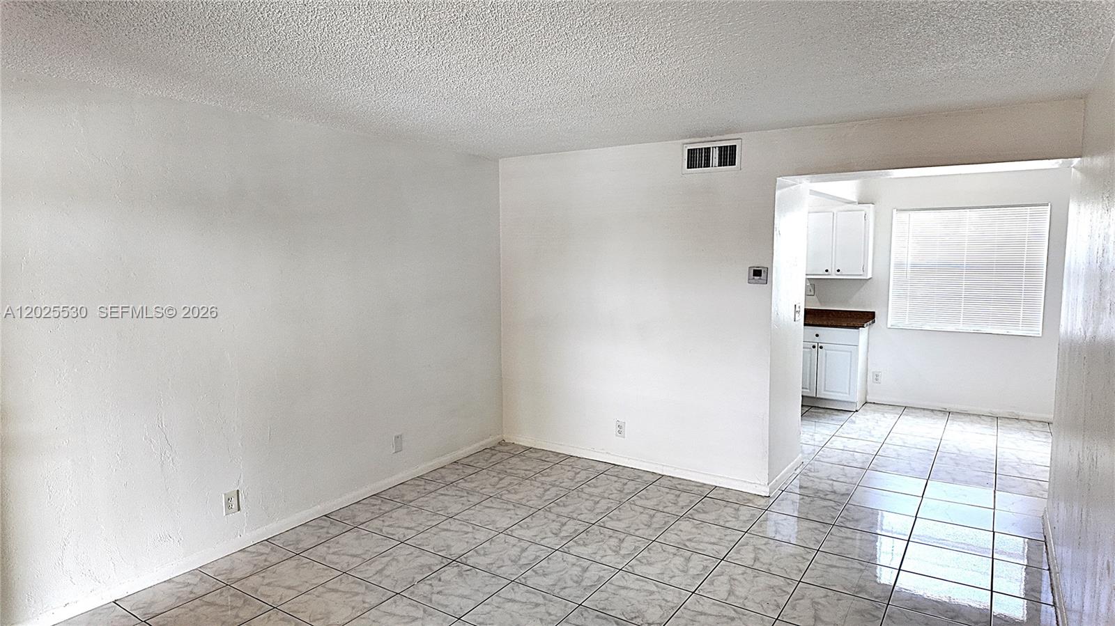 An empty room with white walls and tiled floors leads into a kitchen area — 31 SE 2nd Ave # 203, Hallandale Beach FL 33009, HALLANDALE BEACH, FL