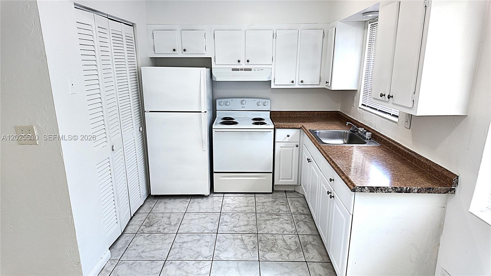 A kitchen features white cabinetry, white appliances, a brown countertop, and light-colored tiled flooring — 31 SE 2nd Ave # 203, Hallandale Beach FL 33009, HALLANDALE BEACH, FL