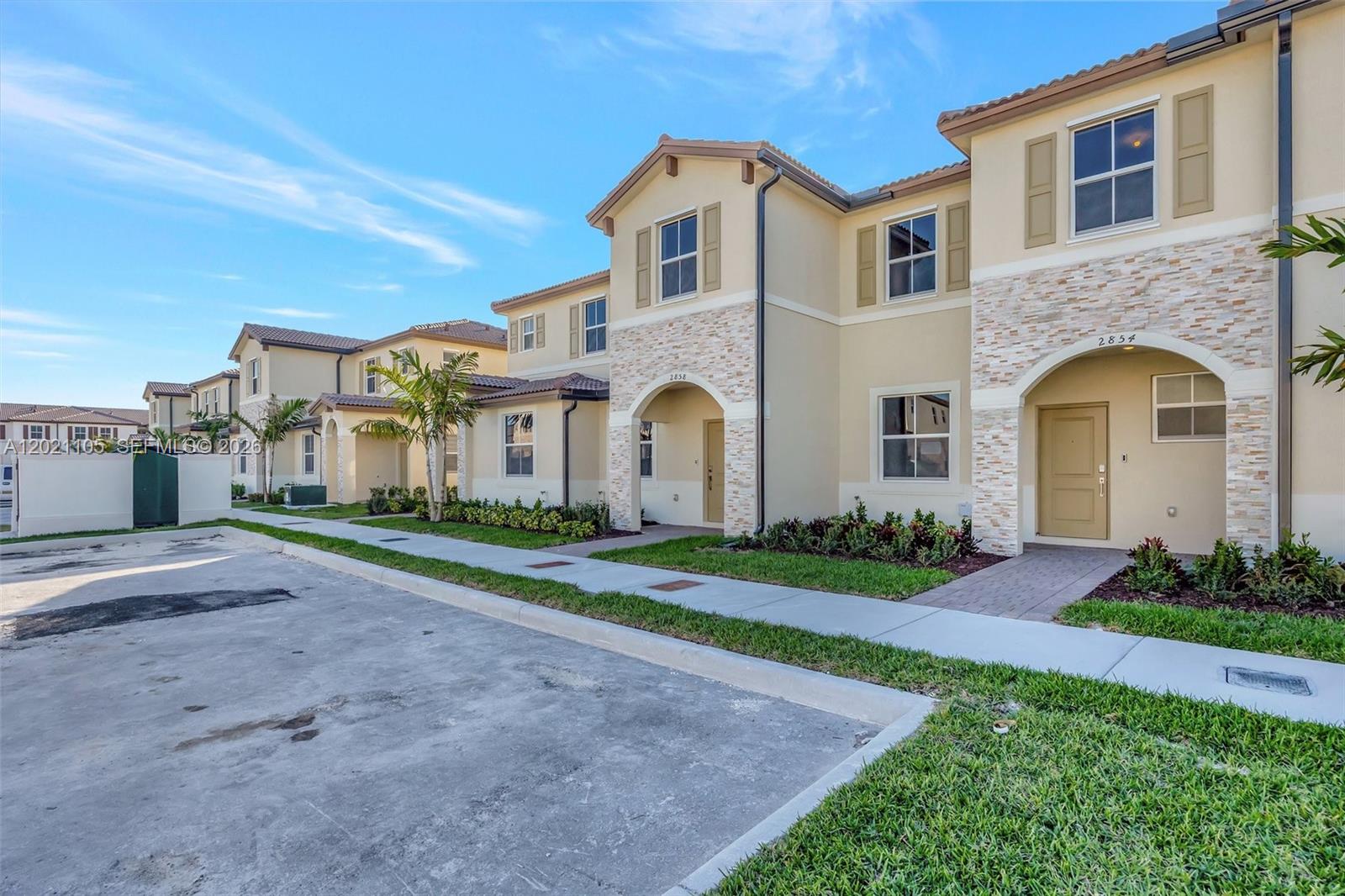 A row of two-story townhomes with beige stucco, stone accents, and tan doors — HOMESTEAD, FL