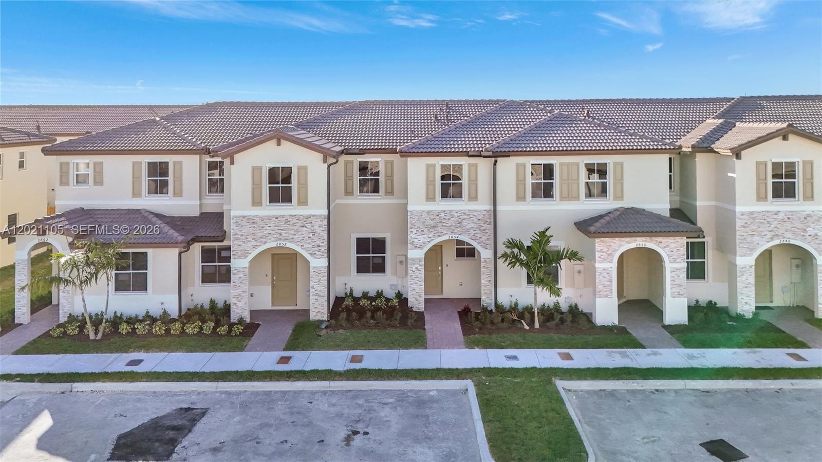 A row of two-story townhomes features beige stucco walls, stone accents, and dark tiled roofs — HOMESTEAD, FL