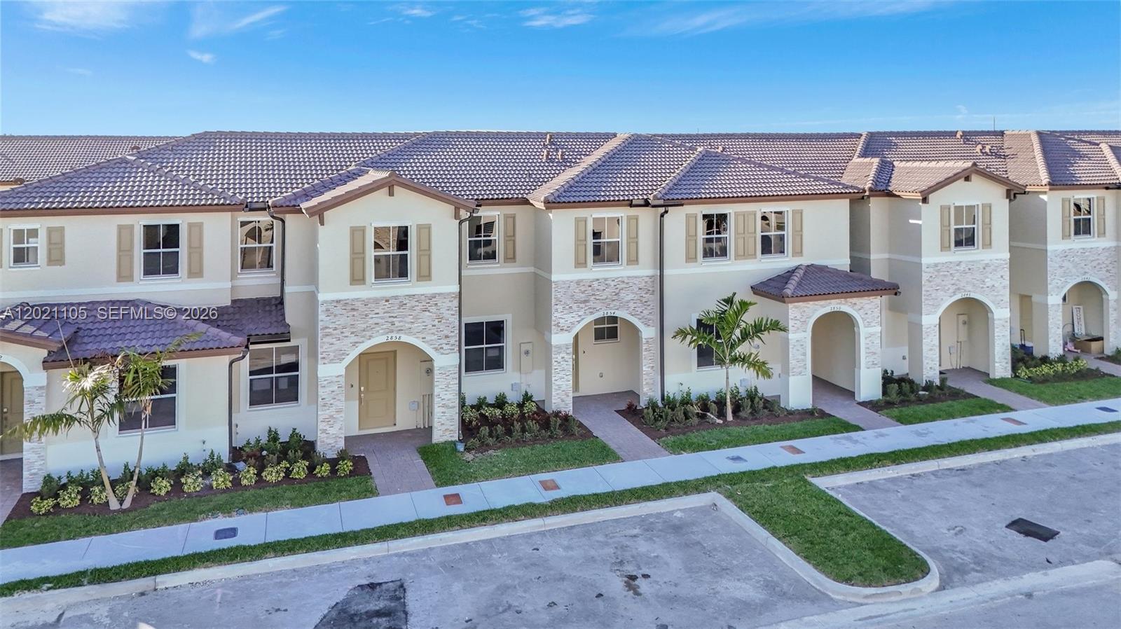 An exterior view of a row of two-story townhouses with tan stucco and stone facades — HOMESTEAD, FL