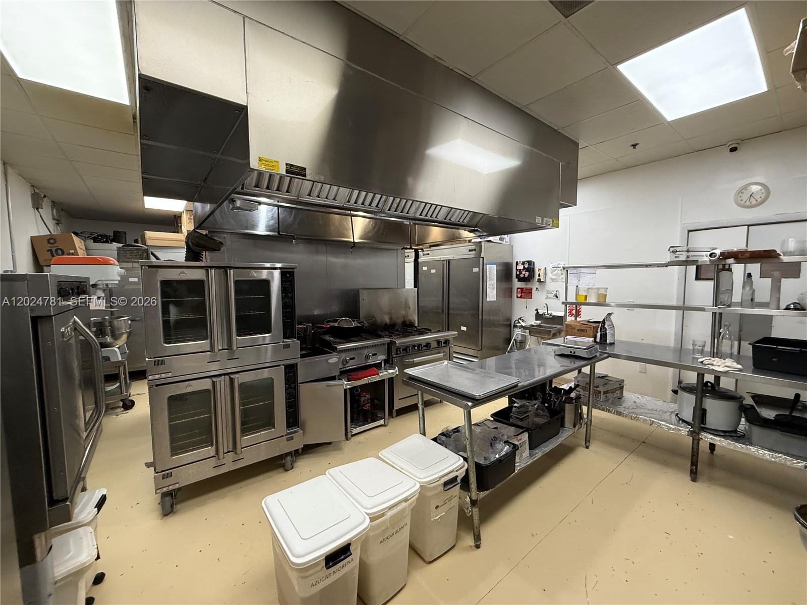 A commercial kitchen features stainless steel appliances, a large ventilation hood, and metal prep tables — PEMBROKE PINES, FL