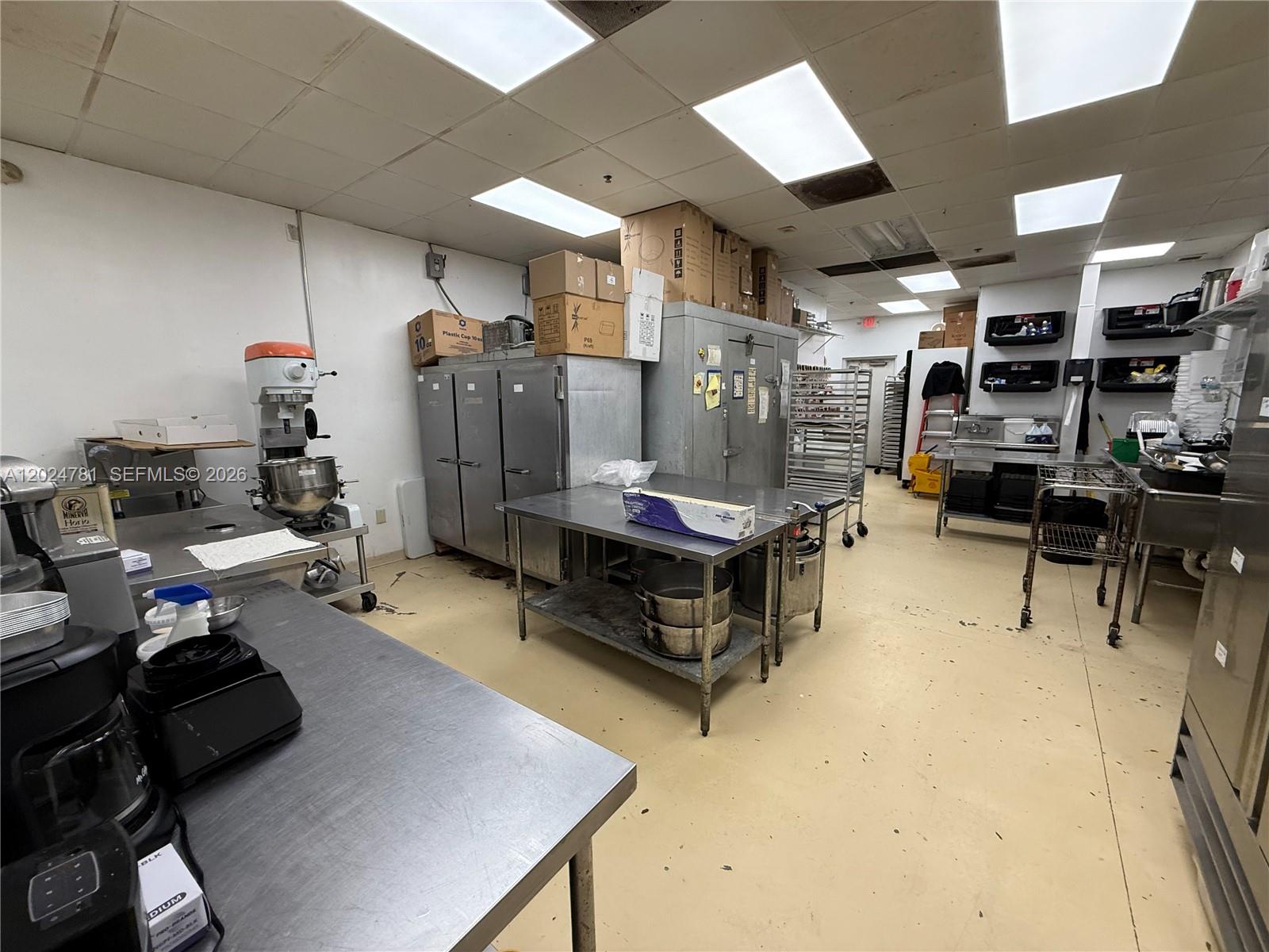 A commercial kitchen features stainless steel prep tables, industrial appliances, and storage shelving — PEMBROKE PINES, FL