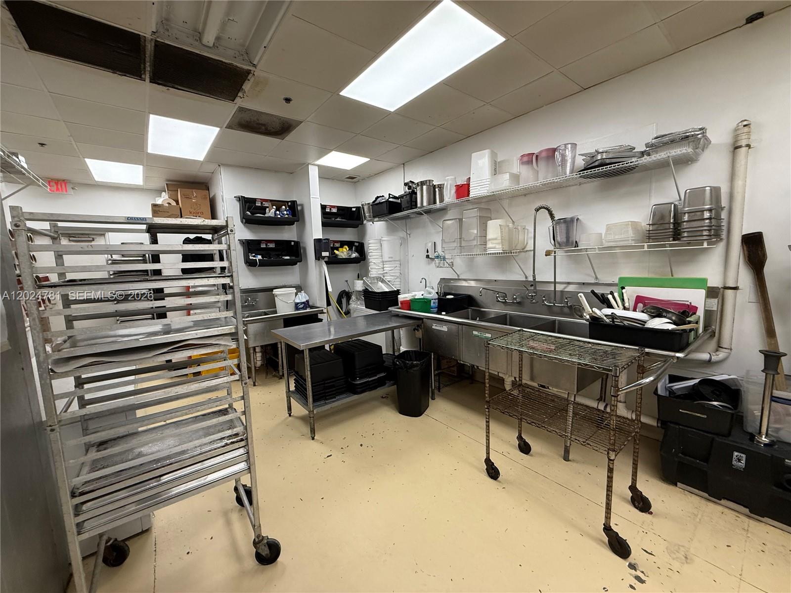 A commercial kitchen features stainless steel sinks, metal shelving, and a rolling rack — PEMBROKE PINES, FL