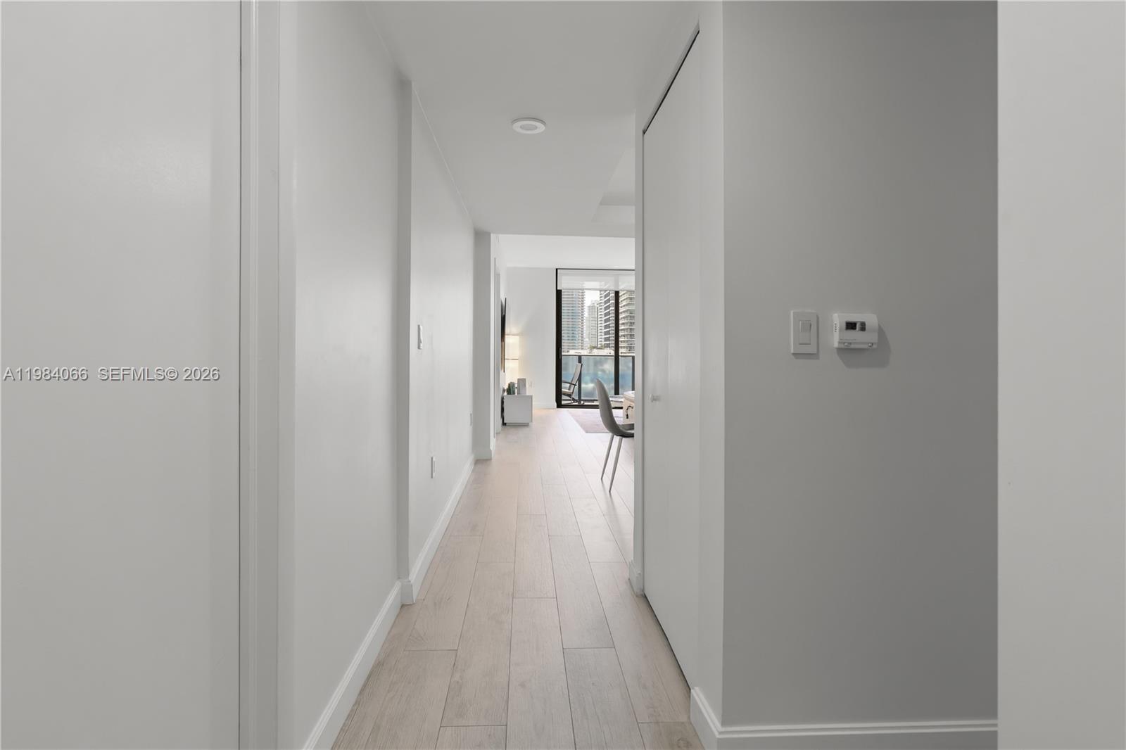 A hallway with light wood-look flooring leads toward a bright living area with balcony views — 45 SW 9th St # 1405, Miami FL 33130, MIAMI, FL