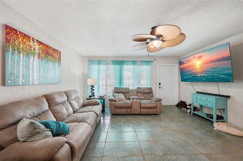 A living room features tile floors, a ceiling fan, two sofas, and a wall-mounted television — 13518 ALBERTA AVENUE, PORT CHARLOTTE, FL