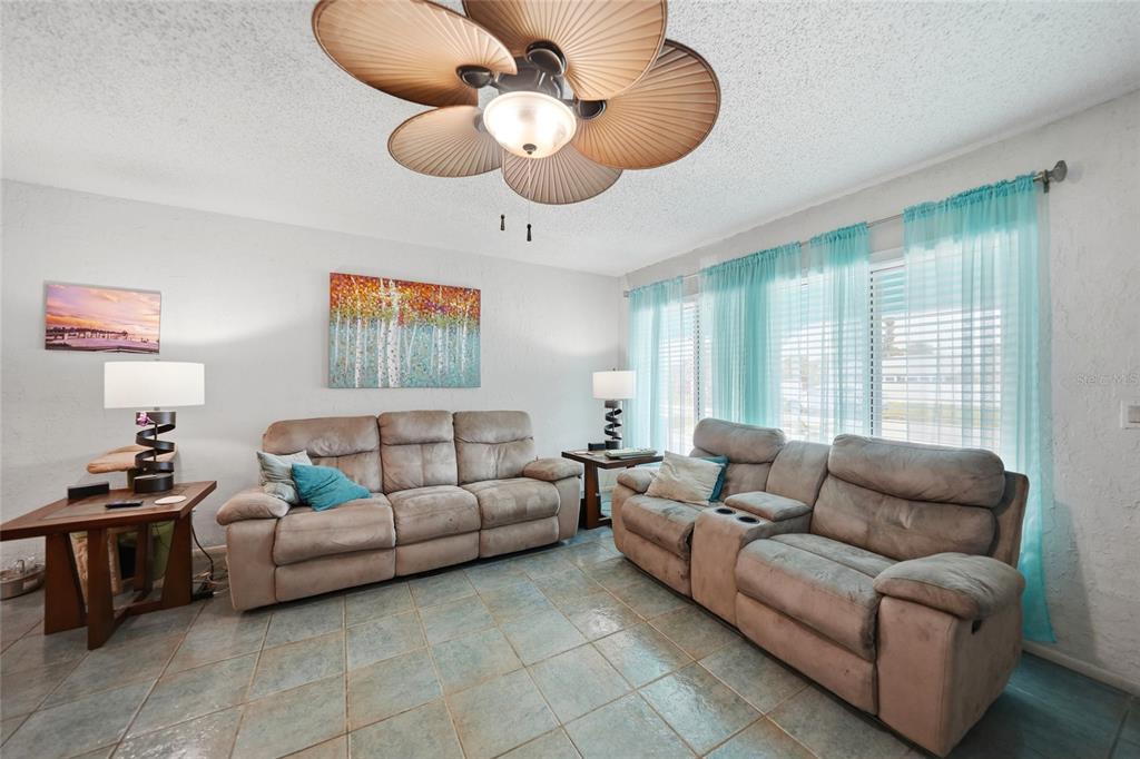 A living room features two beige reclining sofas, a ceiling fan, and light blue curtains — 13518 ALBERTA AVENUE, PORT CHARLOTTE, FL