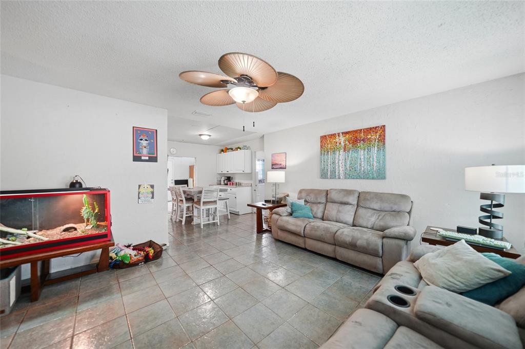 A living room with tile floors, a ceiling fan, and a sofa faces a kitchen — 13518 ALBERTA AVENUE, PORT CHARLOTTE, FL