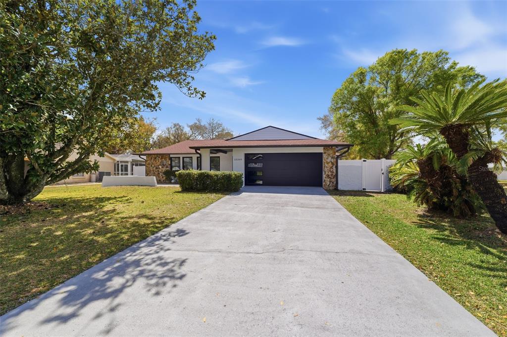 A single-story house with a dark garage door, stone accents, and a concrete driveway — 22368 SOUTHSHORE DRIVE, LAND O LAKES, FL