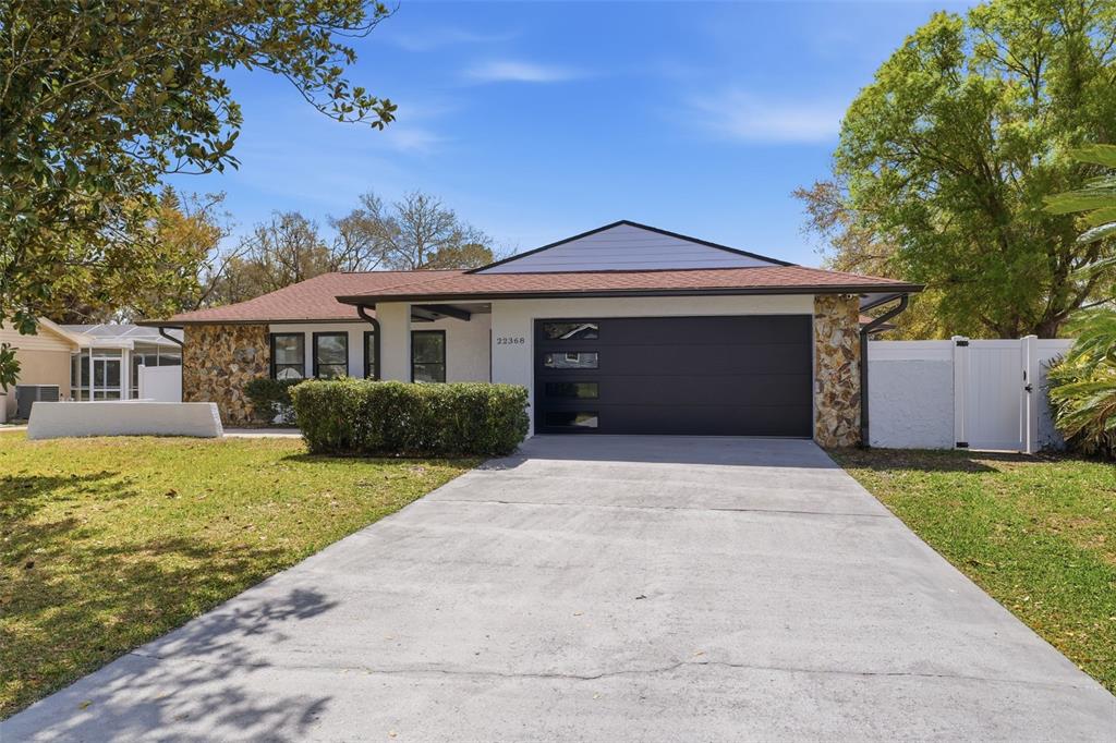 A single-story house with a stone facade, a dark garage door, and a concrete driveway — 22368 SOUTHSHORE DRIVE, LAND O LAKES, FL