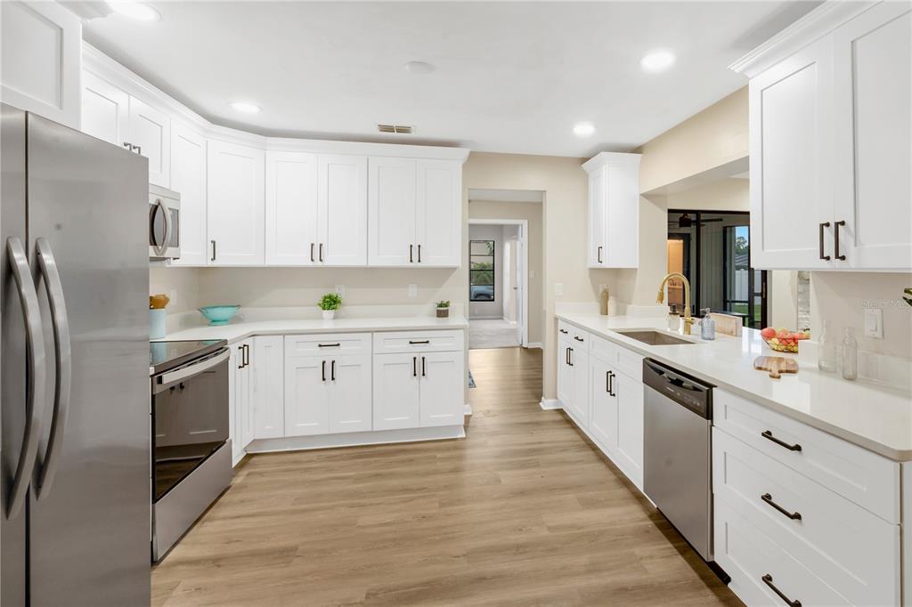 A kitchen features white cabinets, stainless steel appliances, and light wood-look flooring — 2805 BEAGLE PLACE, SEFFNER, FL