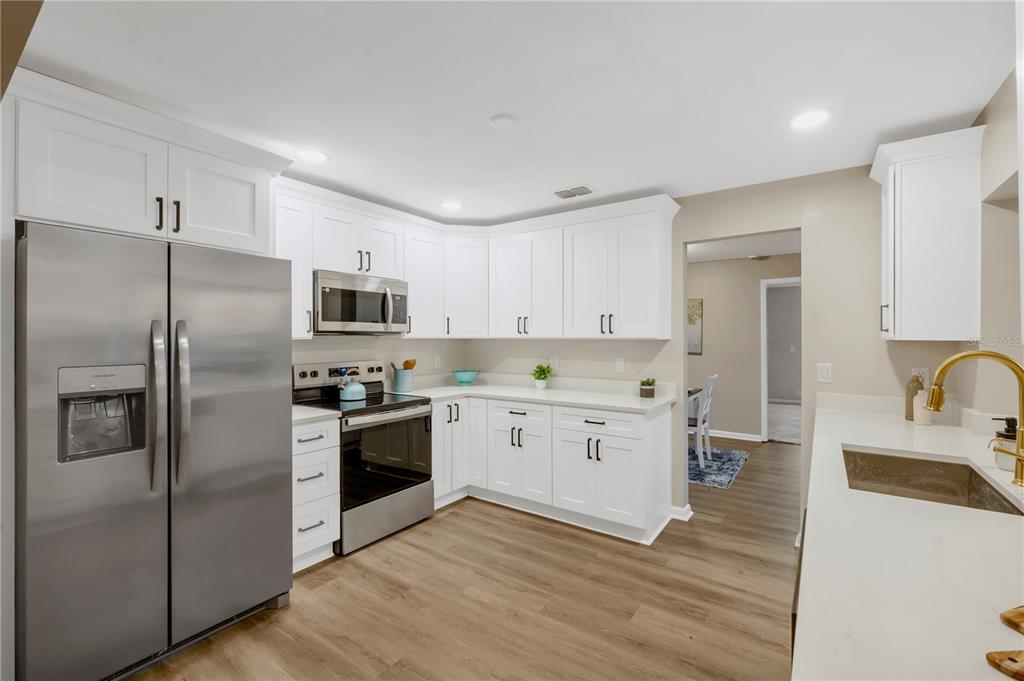 A kitchen features white cabinets, stainless steel appliances, and light wood-look flooring — 2805 BEAGLE PLACE, SEFFNER, FL