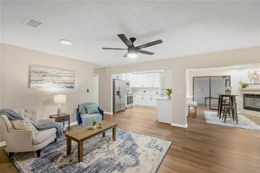 An open-concept living room with wood-look flooring leads into a white kitchen and dining area — 2805 BEAGLE PLACE, SEFFNER, FL