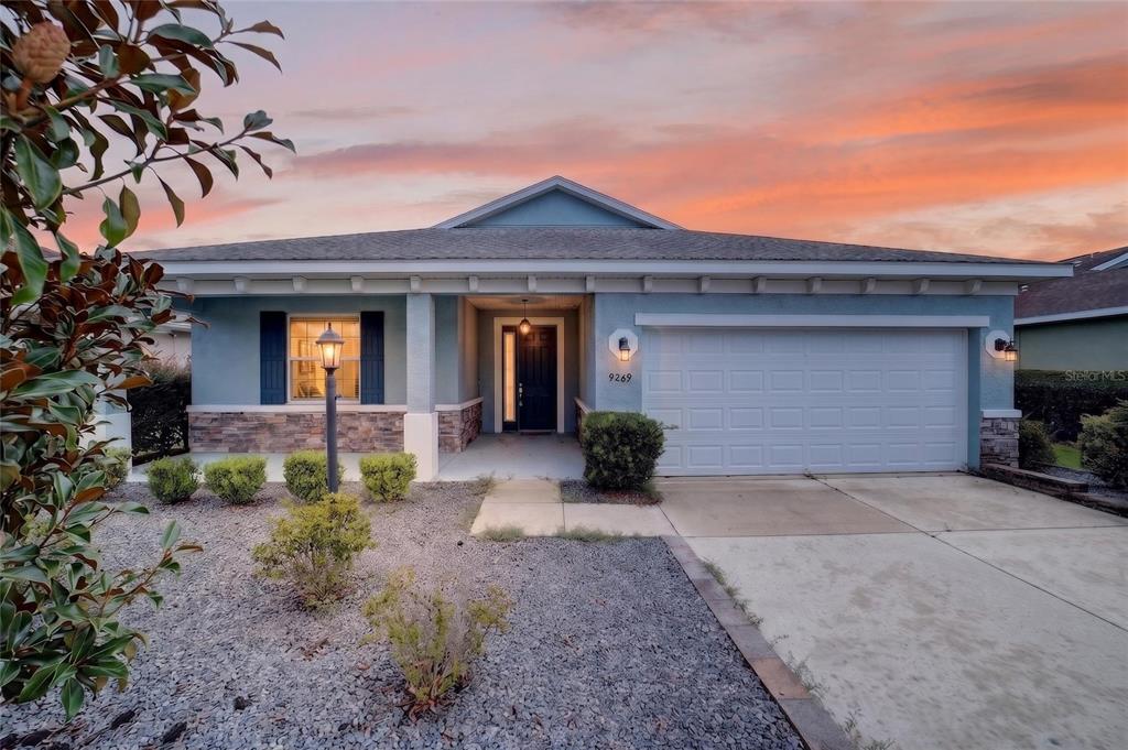 A single-story house with a blue exterior, stone accents, and a two-car garage at sunset — 9269 SW 97TH CIRCLE, OCALA, FL