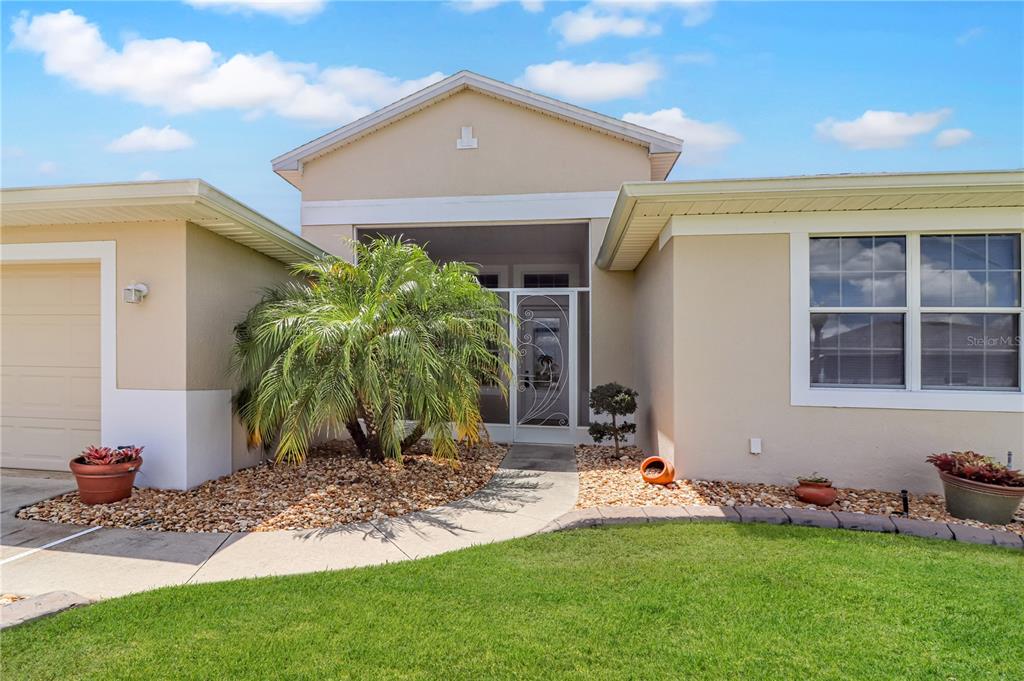 A beige house exterior features a screened entryway, a palm tree, and a front lawn — 27328 PINE STRAW ROAD, LEESBURG, FL