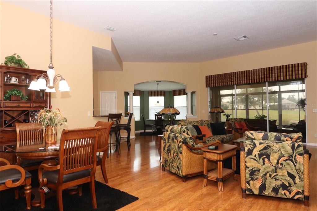 An open-concept living and dining area features hardwood floors, tropical-print furniture, and large sliding doors — 27328 PINE STRAW ROAD, LEESBURG, FL