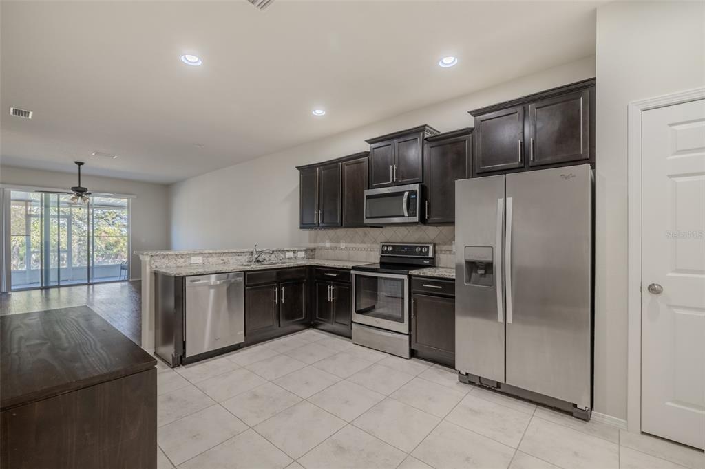 A kitchen features dark wood cabinets, stainless steel appliances, granite countertops, and light tile flooring — 4734 WHITE SANDERLING CT COURT, TAMPA, FL