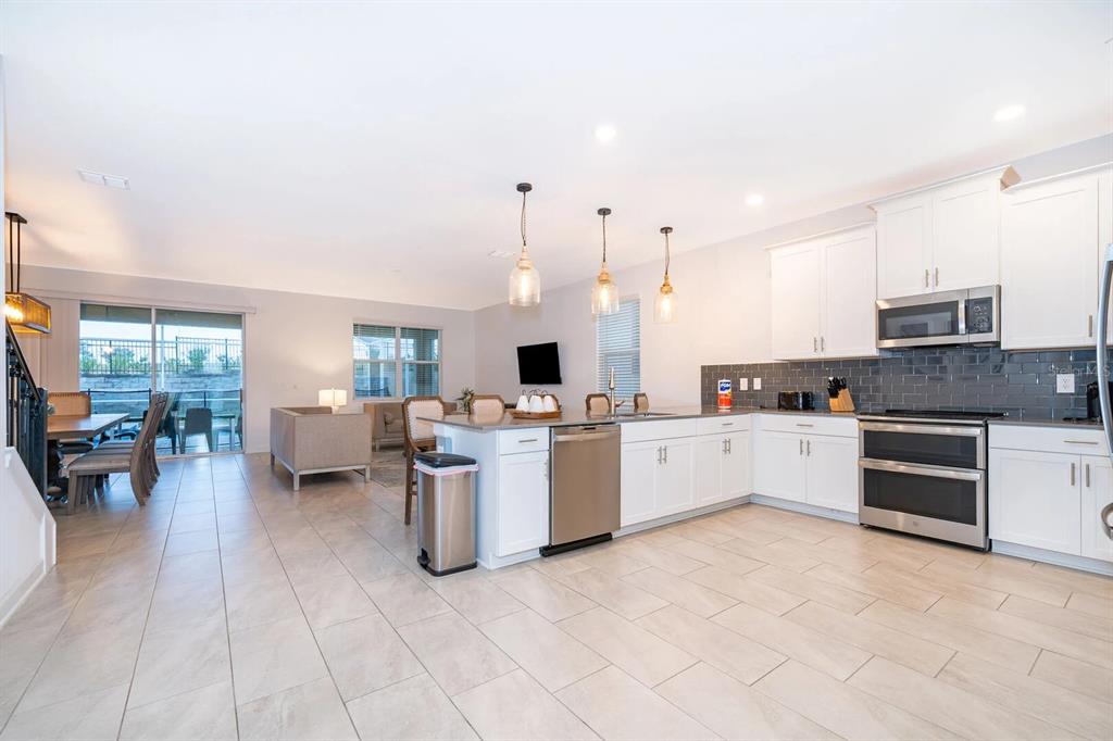 A kitchen with white cabinets, stainless steel appliances, and an island opens to a living area — 9056 SOMMERSET HILLS DRIVE, DAVENPORT, FL