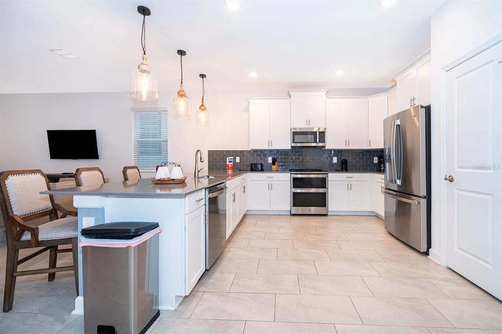A modern kitchen features white cabinets, stainless steel appliances, a gray island, and tile flooring — 9056 SOMMERSET HILLS DRIVE, DAVENPORT, FL