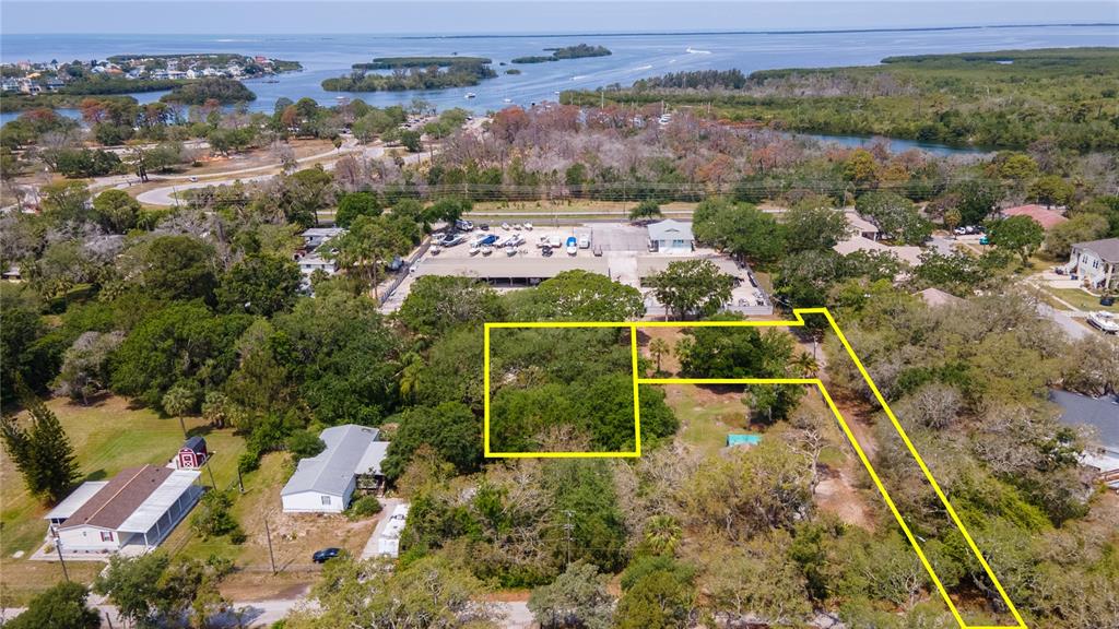 An aerial view shows a wooded residential lot outlined in yellow near a coastal waterway — 1810, 1814 CEMETERY ROAD, HOLIDAY, FL
