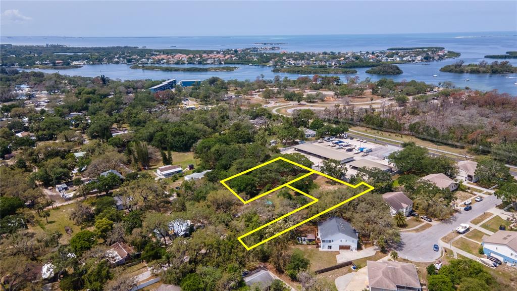 An aerial view shows a vacant, tree-covered lot outlined in yellow near a waterfront community — 1810, 1814 CEMETERY ROAD, HOLIDAY, FL