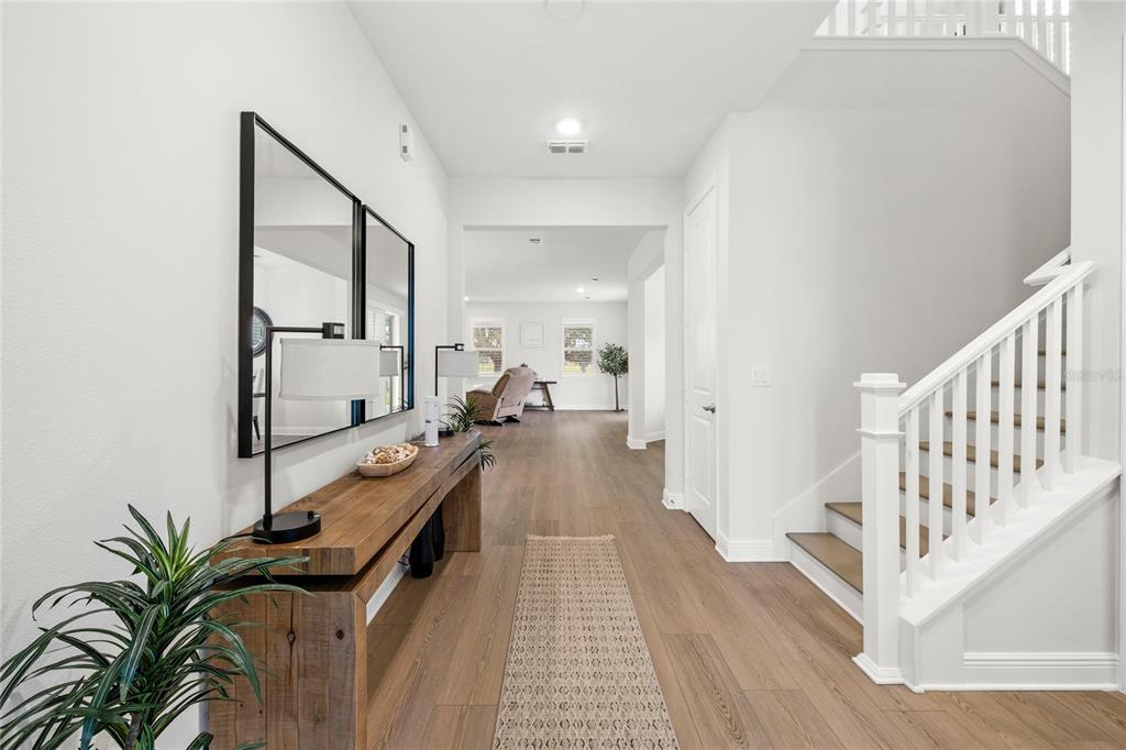 A bright entryway features wood-look flooring, a rustic console table with mirrors, and a staircase — 2985 WATER CLOVER COURT, APOPKA, FL
