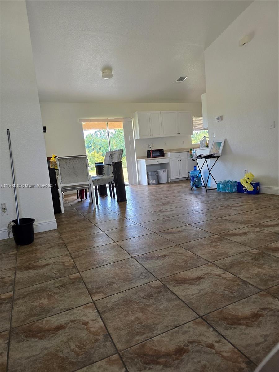 This open-concept living and dining area features tiled floors and a kitchen with white cabinetry — 466 rewing st, Lehigh Acres FL 33974, LEHIGH ACRES, FL