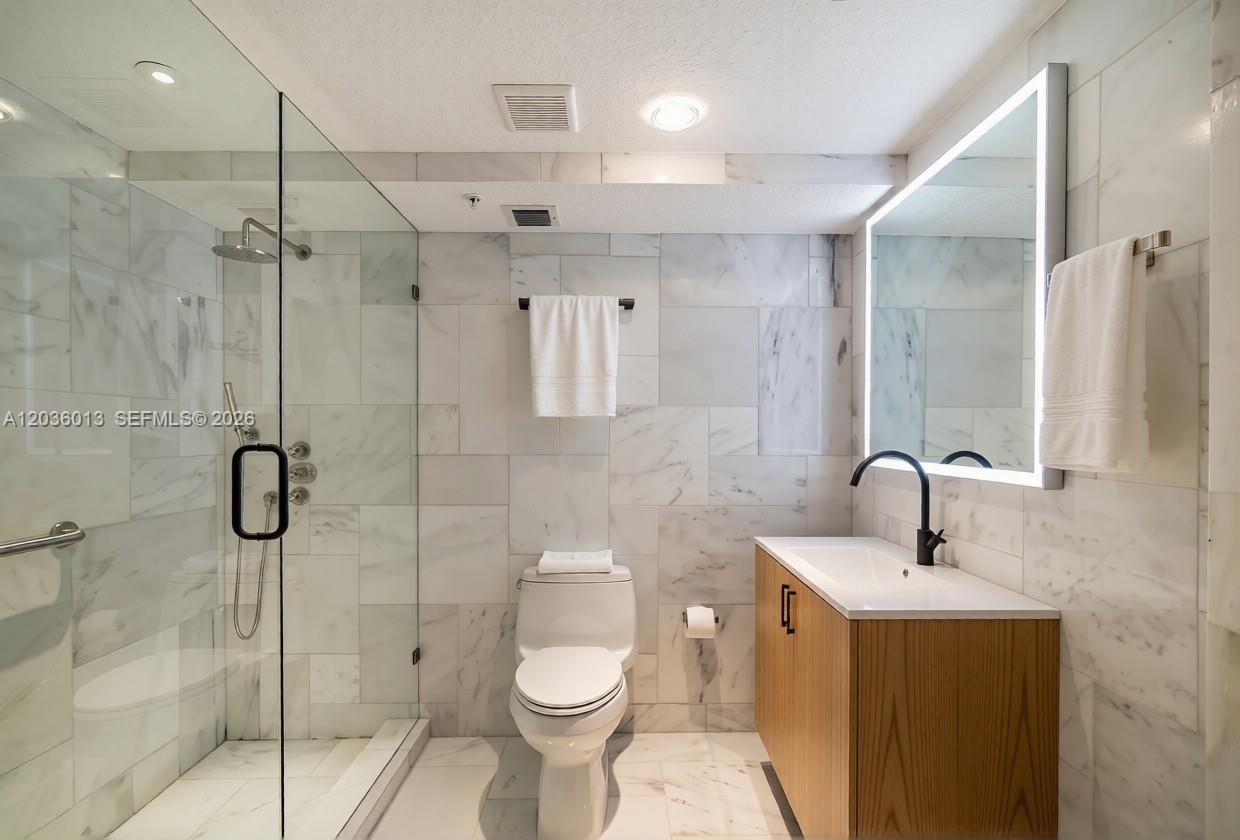 A modern bathroom features marble tile walls, a glass-enclosed shower, and a wood vanity — 322 Buchanan St # 0, Hollywood FL 33019, HOLLYWOOD, FL