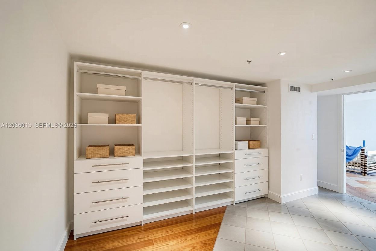 A walk-in closet features white built-in shelving, drawers, and hanging rods with mixed flooring — 322 Buchanan St # 0, Hollywood FL 33019, HOLLYWOOD, FL