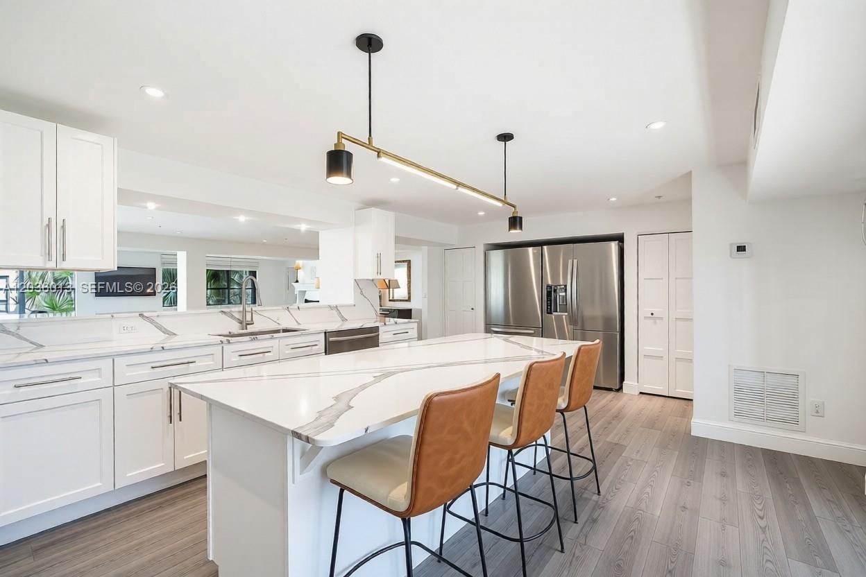A modern kitchen features white cabinetry, a marble-topped island with leather stools, and stainless appliances — 322 Buchanan St # 0, Hollywood FL 33019, HOLLYWOOD, FL