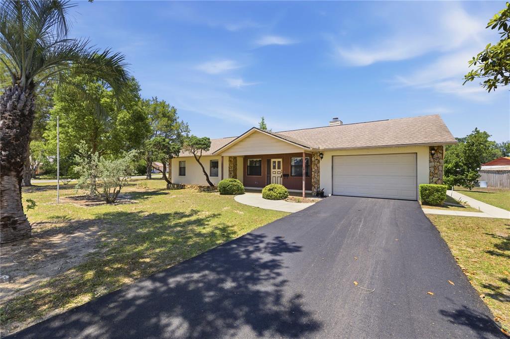 A single-story house with a tan exterior, stone accents, and an asphalt driveway — 3051 SW 98TH STREET ROAD, OCALA, FL