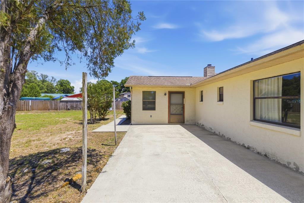 A concrete patio extends from the side of a yellow house toward a grassy yard — 3051 SW 98TH STREET ROAD, OCALA, FL