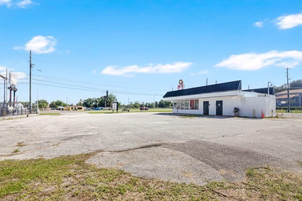 A single-story commercial building sits on a large, paved parking lot under a blue sky — 9710 E COLONIAL DRIVE, ORLANDO, FL