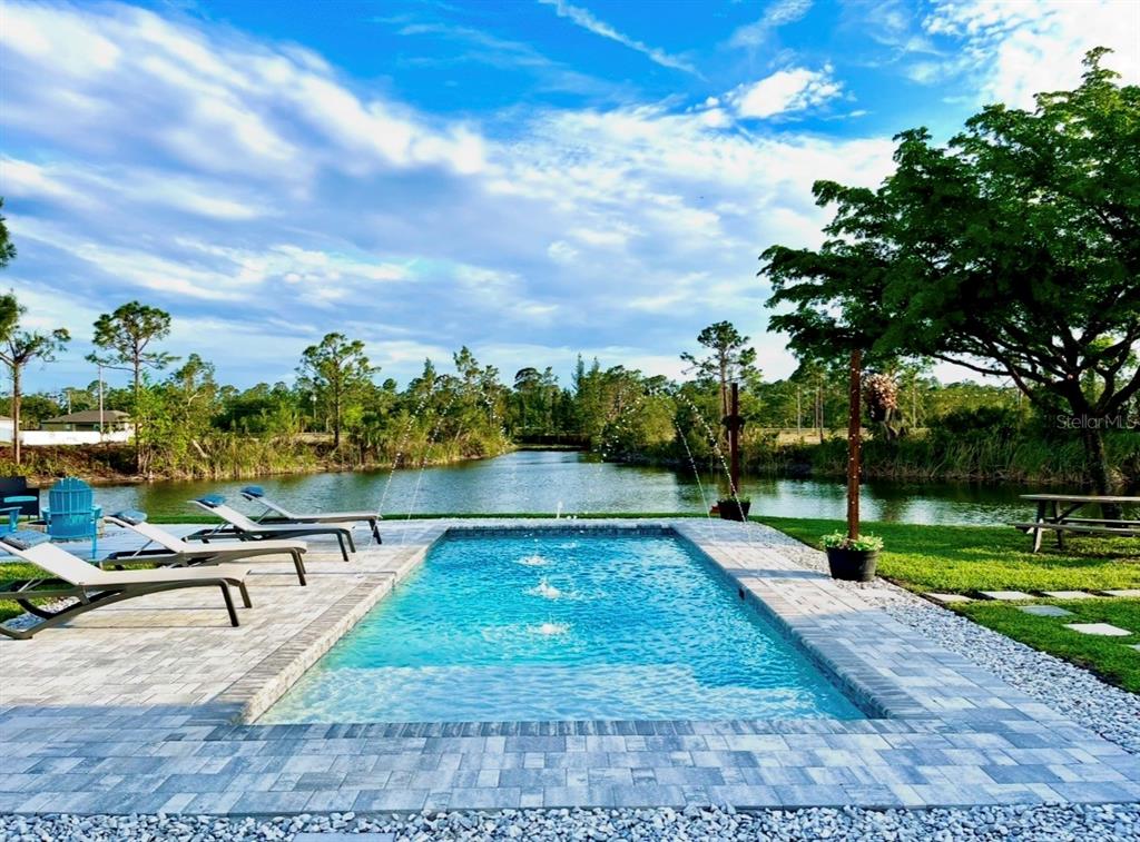 A rectangular swimming pool with fountains sits on a patio overlooking a pond — 2012 NE 33RD LANE, CAPE CORAL, FL