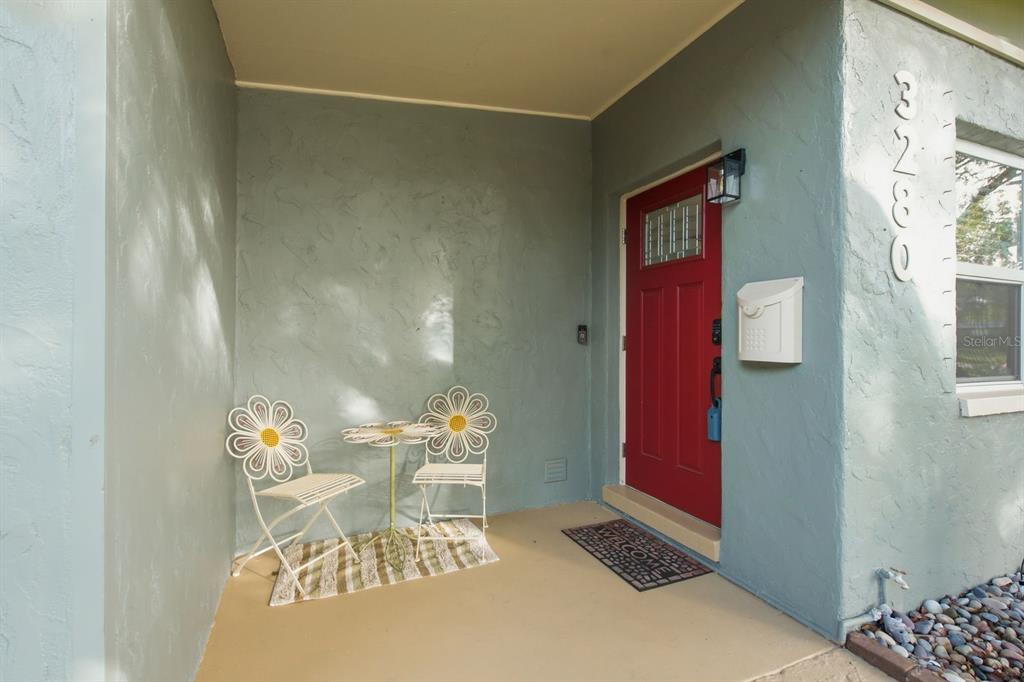 A front porch features a red door, two daisy-shaped chairs, and a small table — 3280 56TH WAY N, ST PETERSBURG, FL