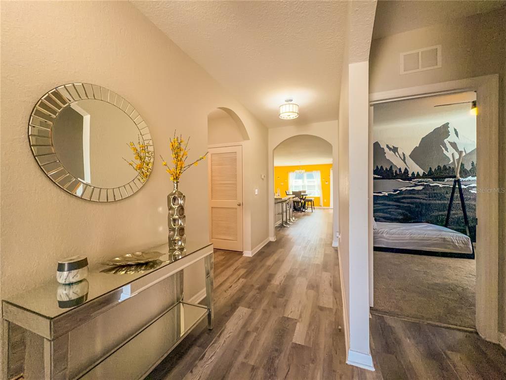 A hallway with wood-look flooring leads to a kitchen, featuring a mirrored console table — 1742 VAN GOGH DRIVE, AUBURNDALE, FL