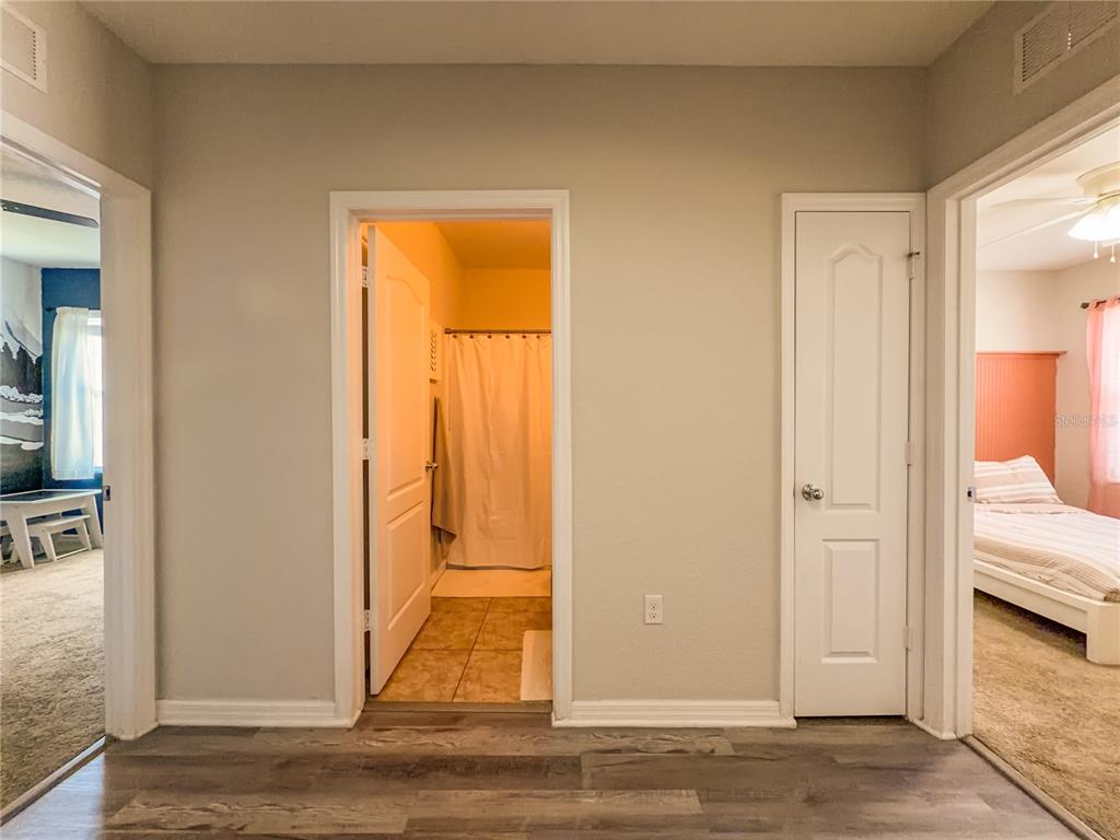 A hallway with wood-look flooring leads to a bathroom and two adjacent bedrooms — 1742 VAN GOGH DRIVE, AUBURNDALE, FL