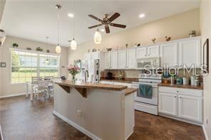 A kitchen features white cabinets, a wooden breakfast bar, and a dining area with windows — 17951 SE 115TH CIRCLE, SUMMERFIELD, FL