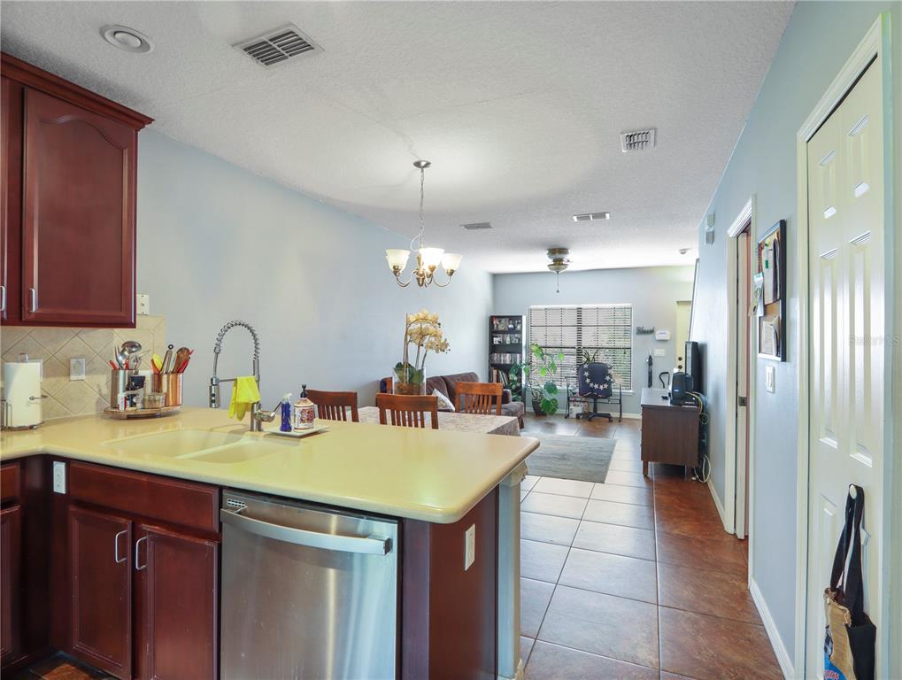 A kitchen with dark wood cabinets and a light countertop overlooks a dining and living area — 3250 WINDLESHORE, SANFORD, FL