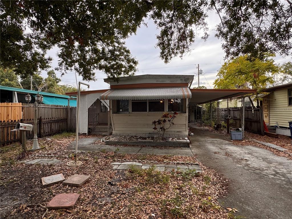 A single-story mobile home with a metal awning, carport, and a leaf-covered front yard — 5042 76TH STREET N, ST PETERSBURG, FL