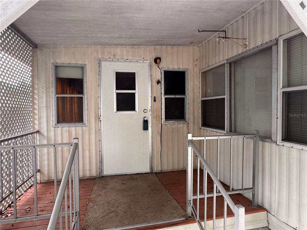 A covered porch features a white door, metal railings, and wood-look flooring — 5042 76TH STREET N, ST PETERSBURG, FL