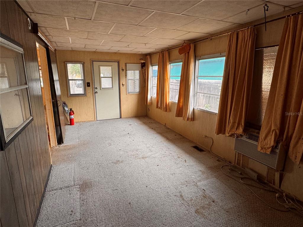 A sunroom with wood-paneled walls, carpeted flooring, multiple windows, and a window air conditioning unit — 5042 76TH STREET N, ST PETERSBURG, FL