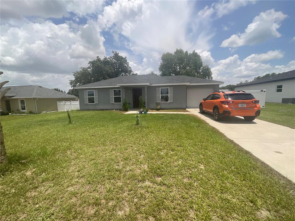 A gray single-story house with a concrete driveway and an orange car parked in front — 15309 SW 52ND CIRCLE, OCALA, FL